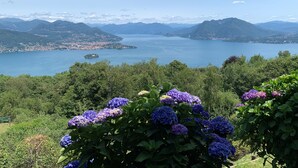 A scenic view of a lake with mountains in the background and purple hydrangea flowers in the foreground. - Panoramic View of Lake Maggiore Near Stresa • Private Garden & Parking (Levo di Stresa)