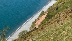 Un paysage côtier avec une plage, des collines verdoyantes et une vue dégagée sur l’océan.