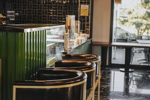 Una zona de bar con mostrador verde y taburetes negros.