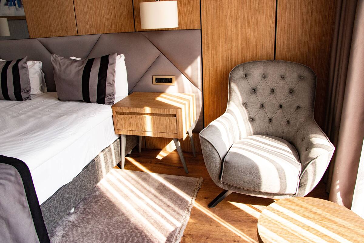Una habitación de hotel moderna con una cama grande, una mesita de noche, una silla y piso de madera.