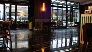 A spacious lobby with a polished marble floor, large windows offering views of the outside, and a seating area with wooden chairs and tables.