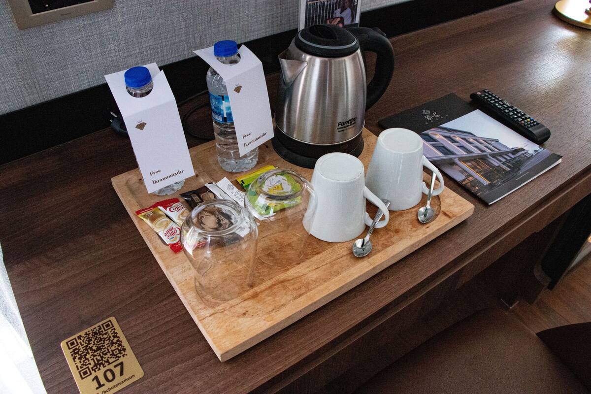 Zona de recepción de un hotel con un mostrador de madera que exhibe comodidades como hervidor, botella de agua, café y un control remoto.