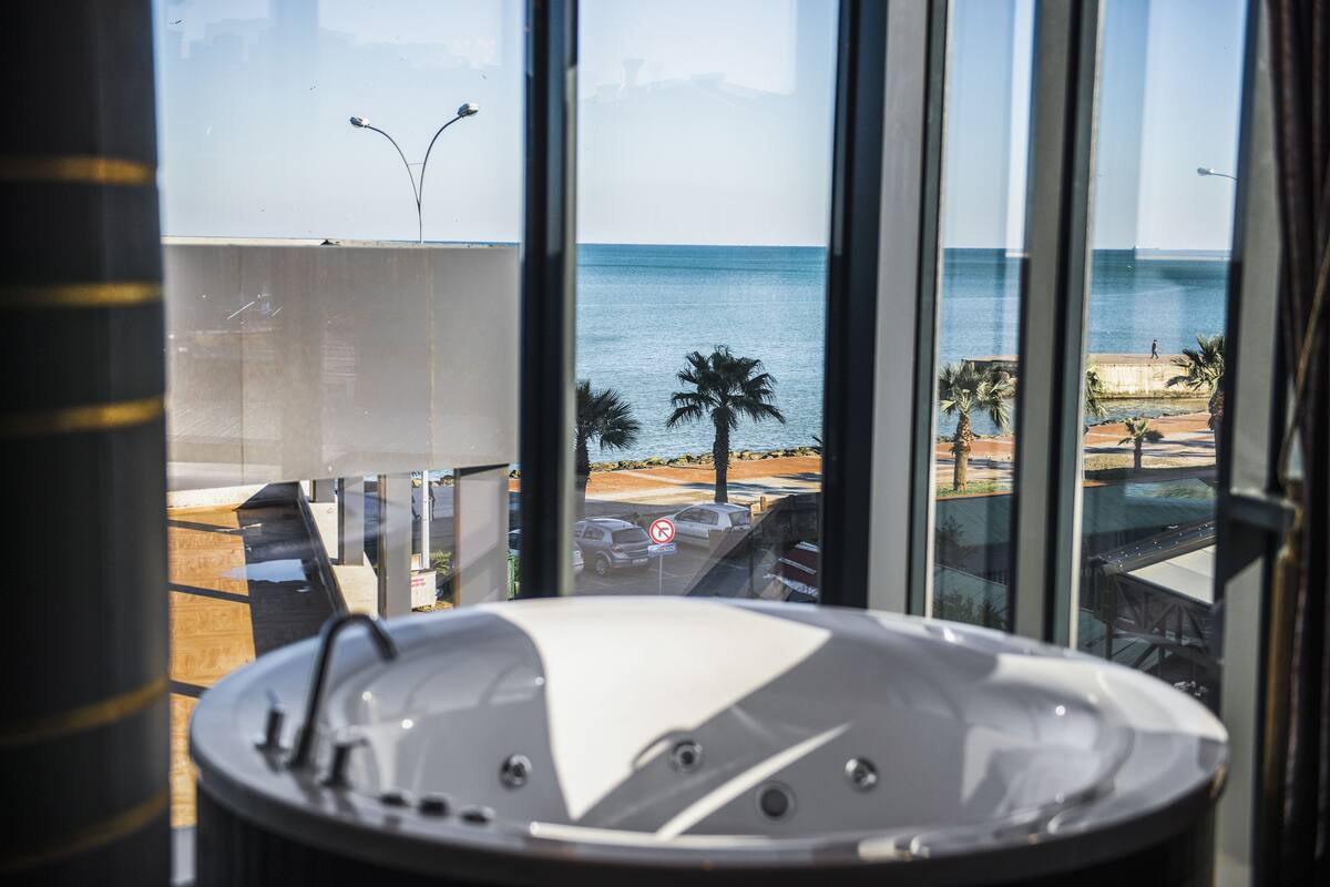Un baño moderno con una bañera grande, vistas al mar y un balcón con mobiliario exterior.