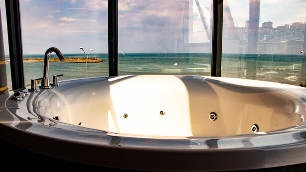 A large bathtub with a view of the ocean and a bridge in the background.