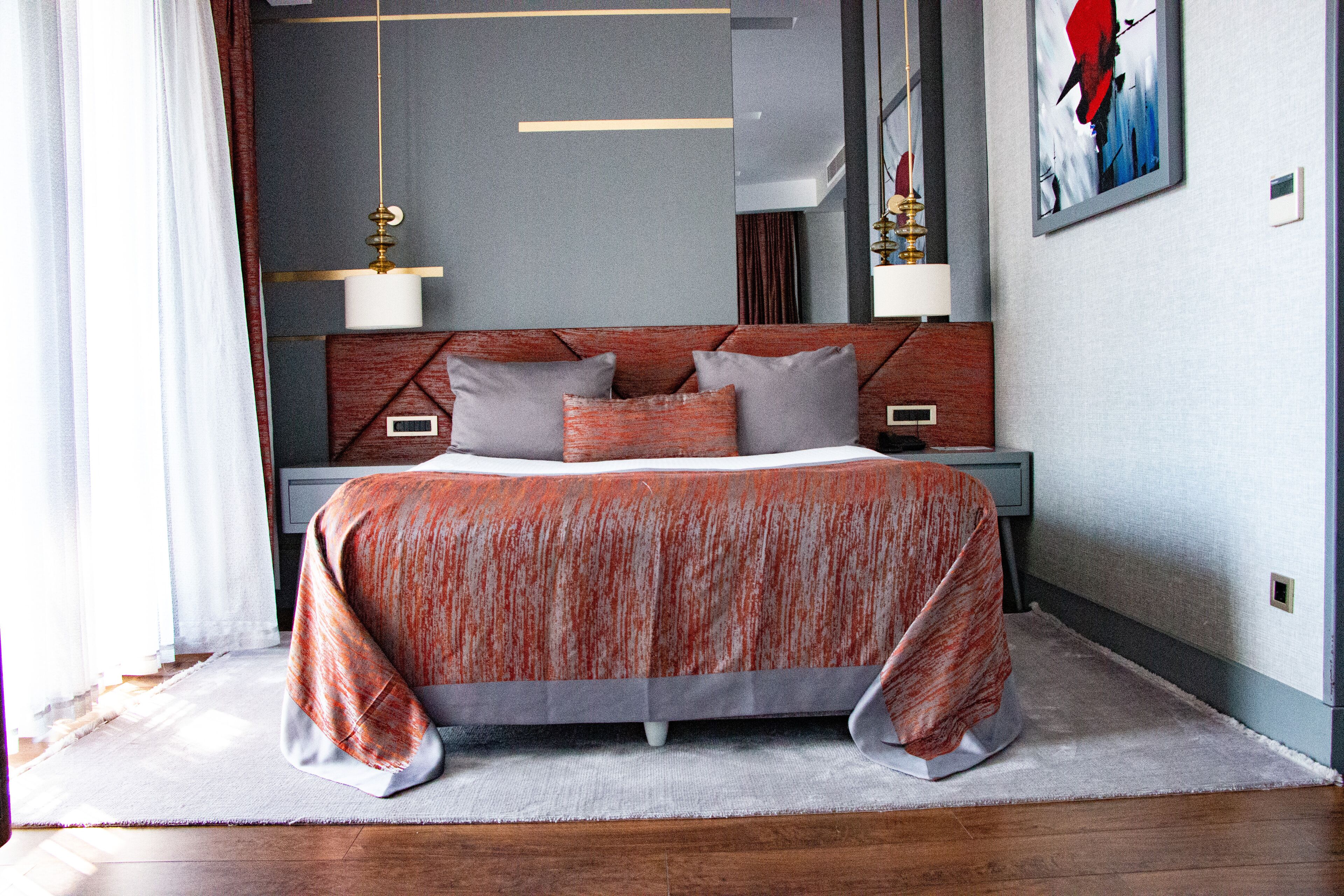A modern bedroom with a large bed, a headboard with geometric patterns, bedside lamps, and a framed artwork on the wall.