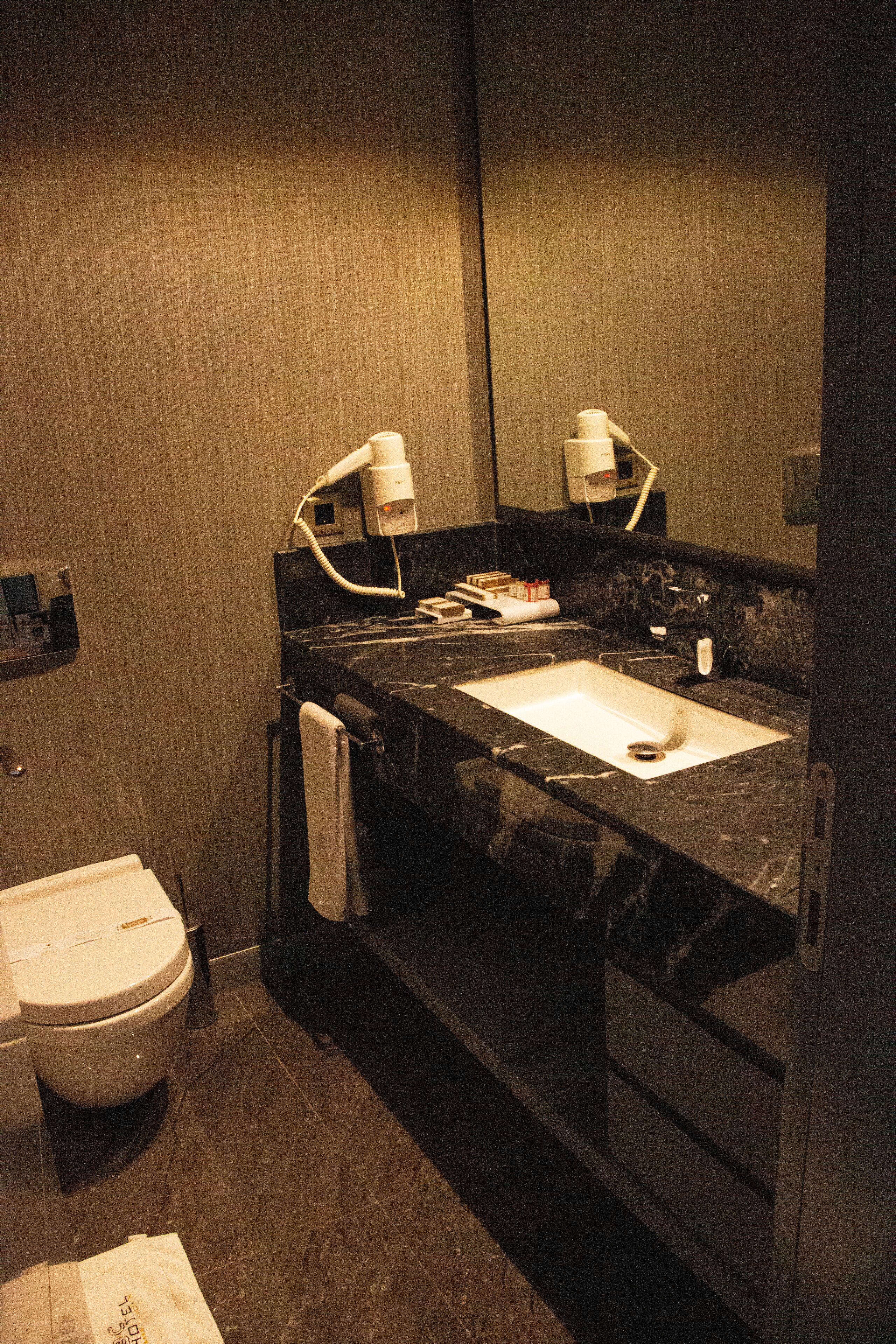 A bathroom with a dark marble sink, a white toilet, a towel hanging on the wall, and a mirror above the sink.