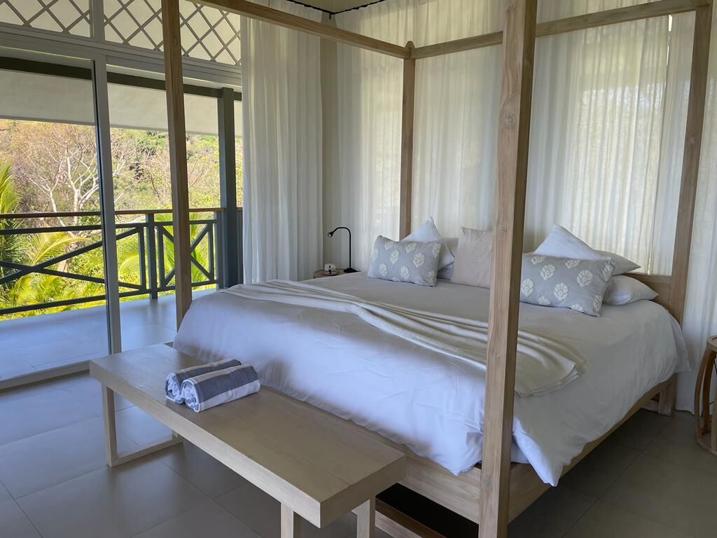 A four-poster bed with a wooden frame, white bedding, and a bench at the foot of the bed.