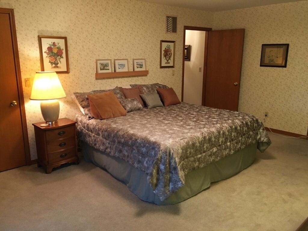 Ein Schlafzimmer mit einem Bett, einem Nachttisch, einer Lampe und einer Tür.