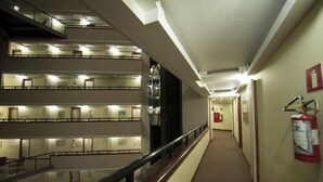 Pasillo de hotel de varios niveles con extintor en la pared, barandilla y señal de salida de incendios.
