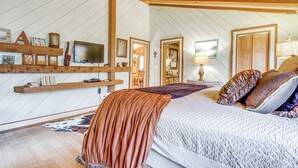 Ein Schlafzimmer mit Holzboden, einem Bett mit gemustertem Überwurf, einem Fernseher und Wandregalen mit verschiedenen Gegenständen.