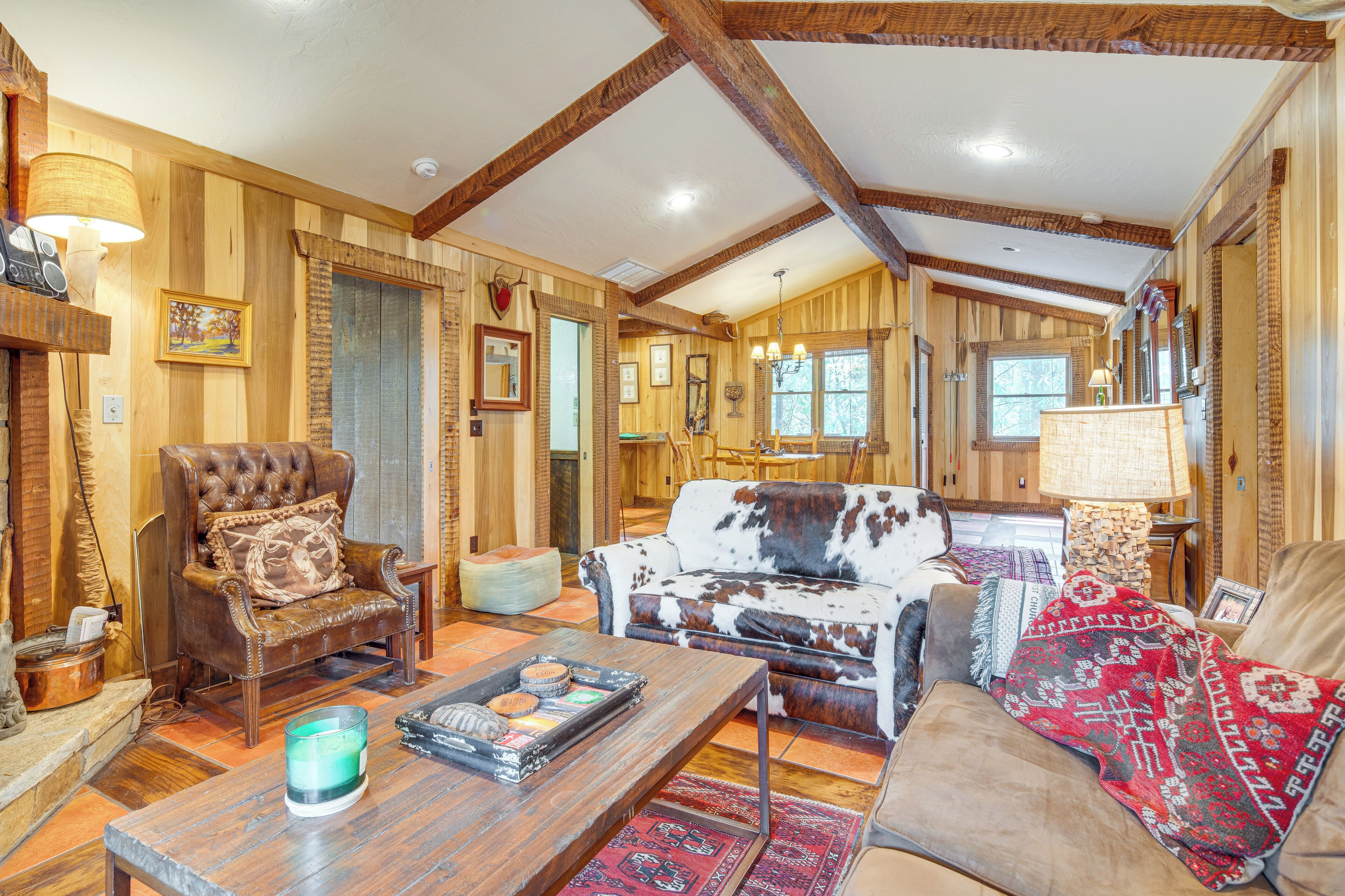 Un salon chaleureux avec des murs en bois, un fauteuil en cuir, un canapé en peau de vache et une table basse agrémentée d’objets décoratifs.