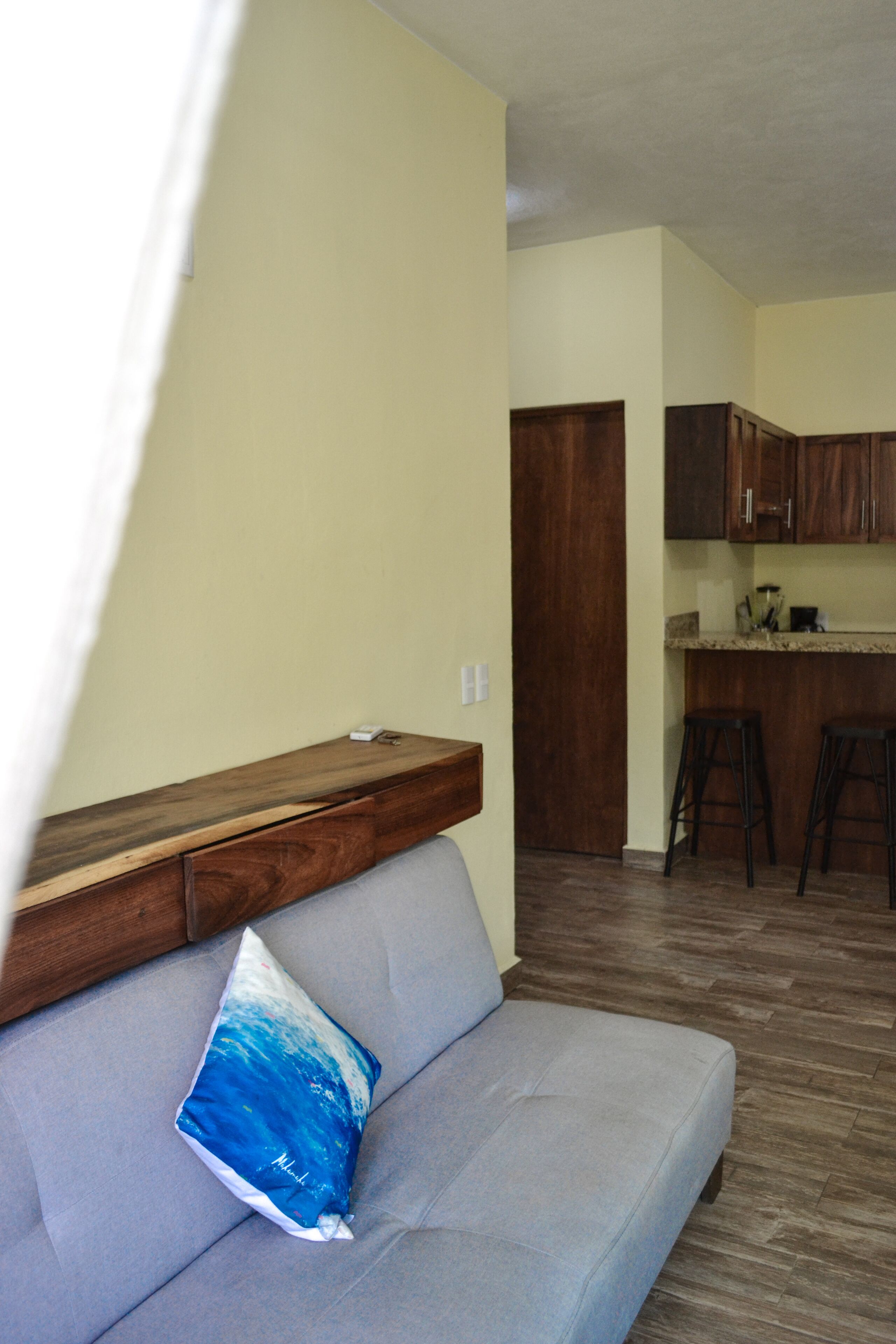 A living room with a grey sofa, a wooden bench, and a kitchen area in the background.