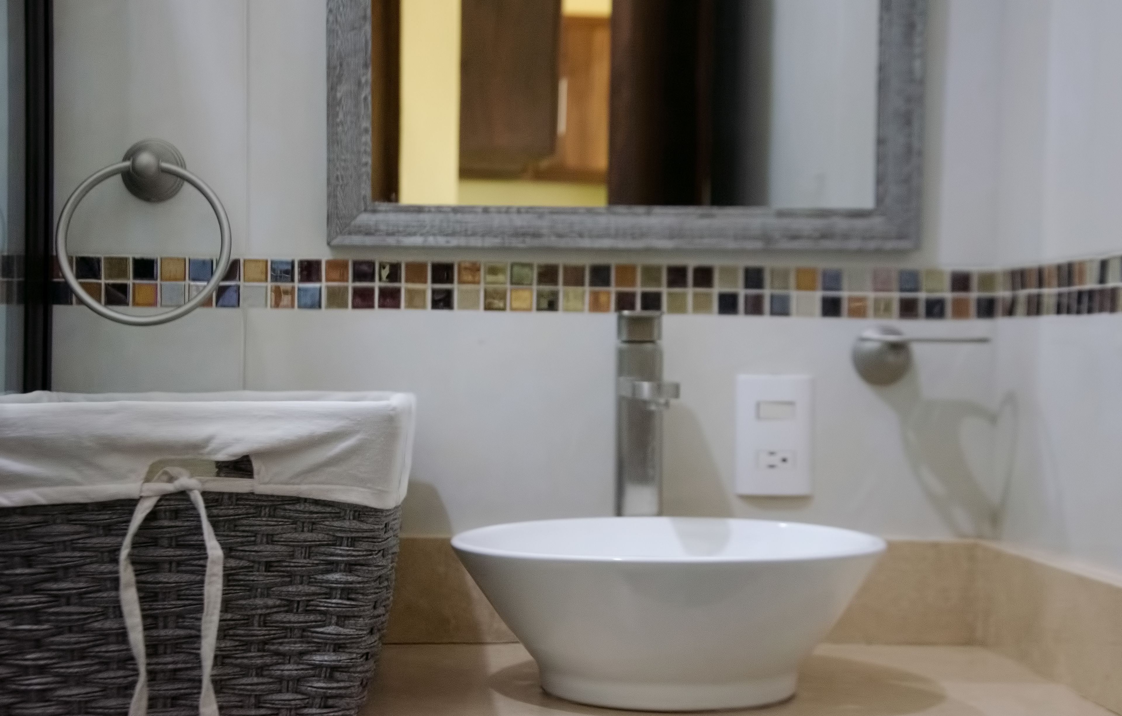 A bathroom with a white sink, a mirror, and a mosaic tile border.