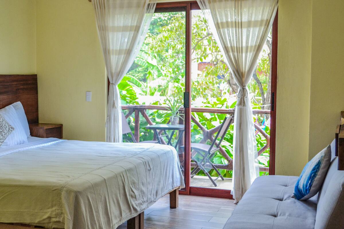 A bedroom with a bed, a sofa, and a balcony with a table and chairs.