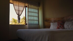 Una camera da letto con un letto, una finestra con tende e vista su palme.
