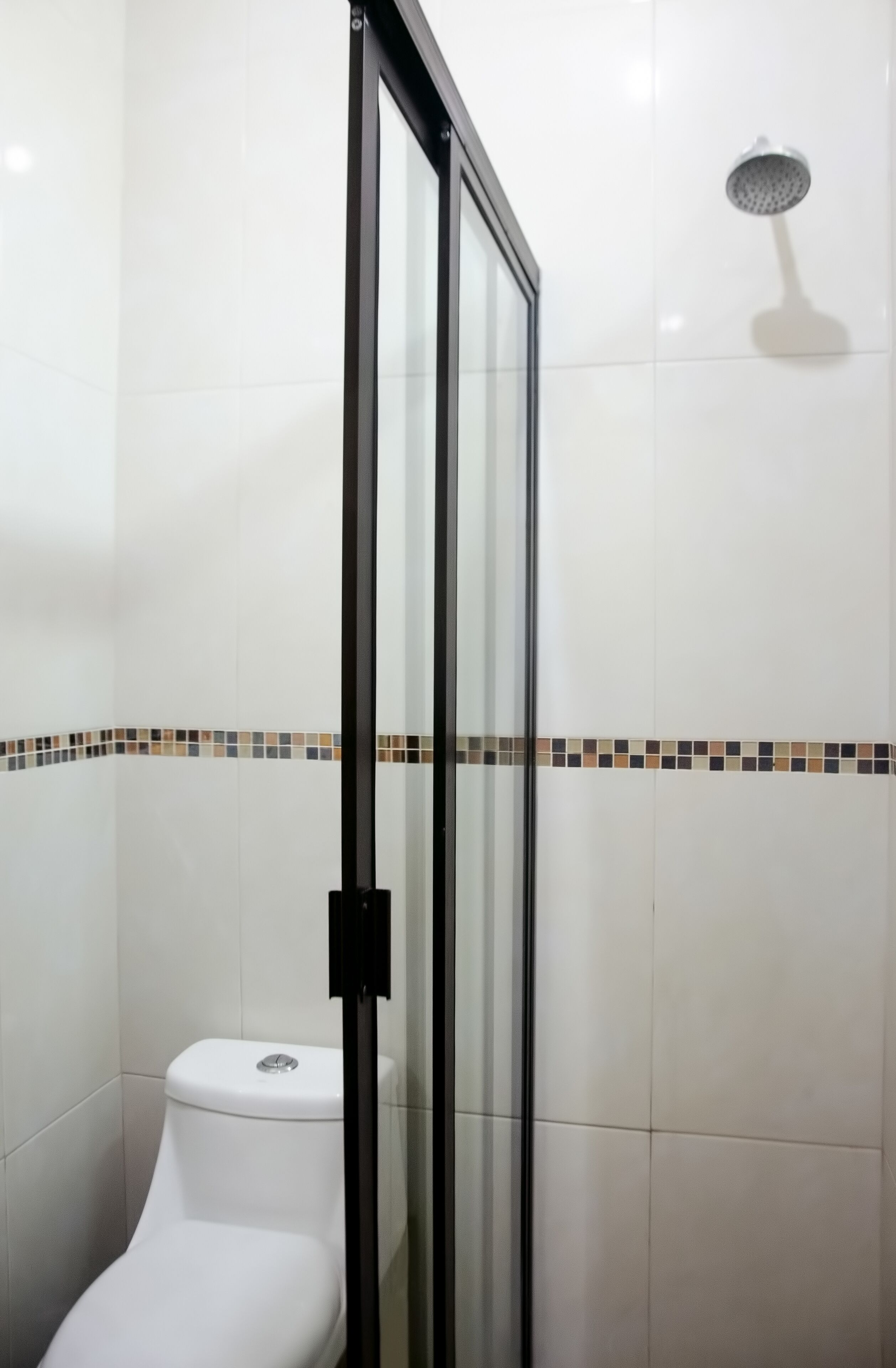 Un baño con cabina de ducha de vidrio, inodoro y pared con zócalo decorativo.
