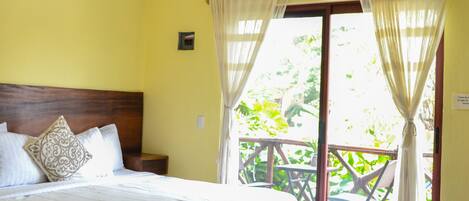 A hotel room with a bed, a sofa, a ceiling fan, and a balcony with curtains.