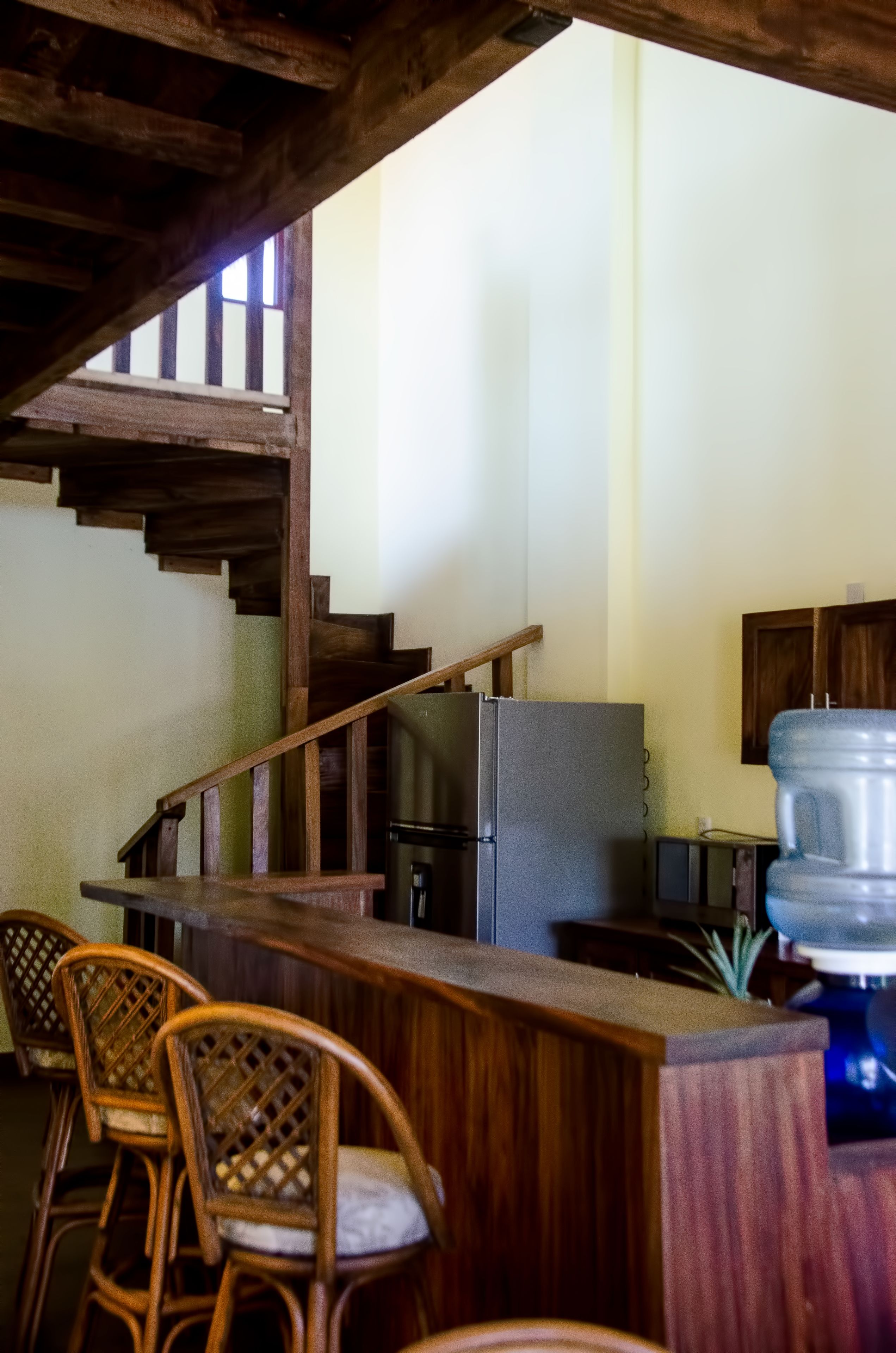 A kitchen with wooden chairs, a bar counter, a refrigerator, and a water dispenser.
