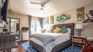 Une chambre dotée d’un grand lit, d’un ventilateur de plafond, d’une télévision, d’un bureau et d’une petite kitchenette.