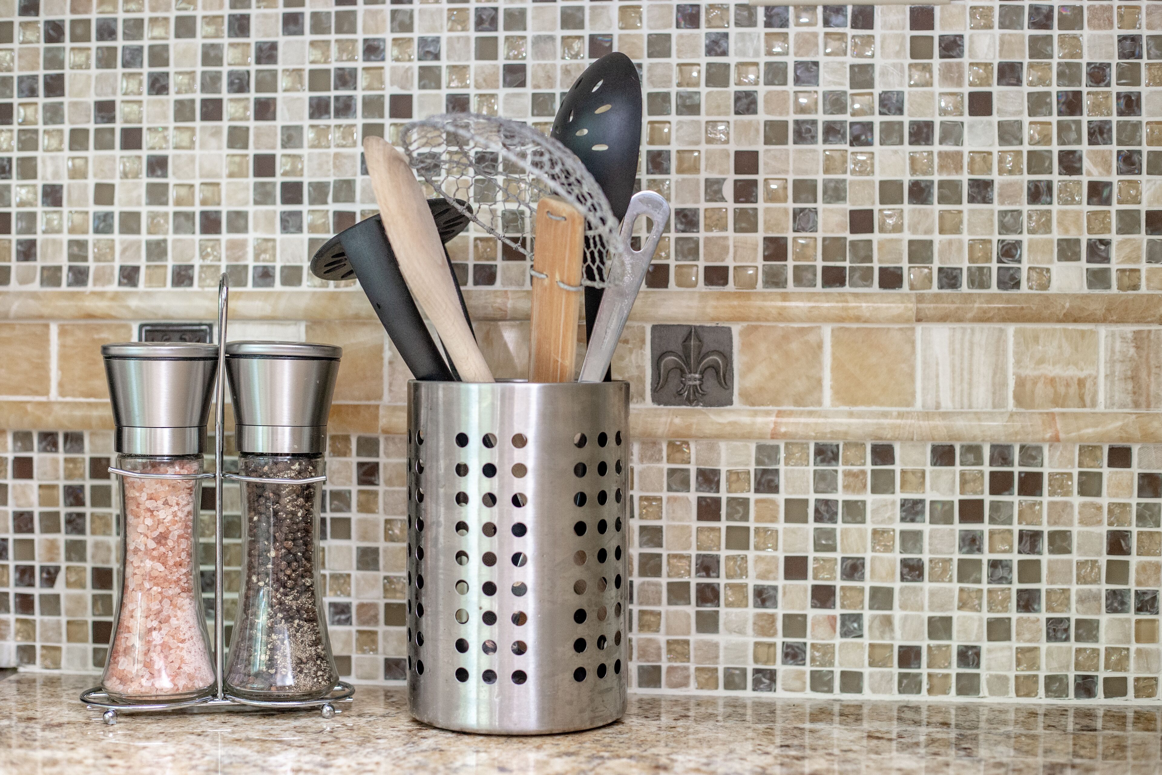 Una encimera de cocina con saleros, un recipiente perforado con utensilios de cocina y un salpicadero azulejado.