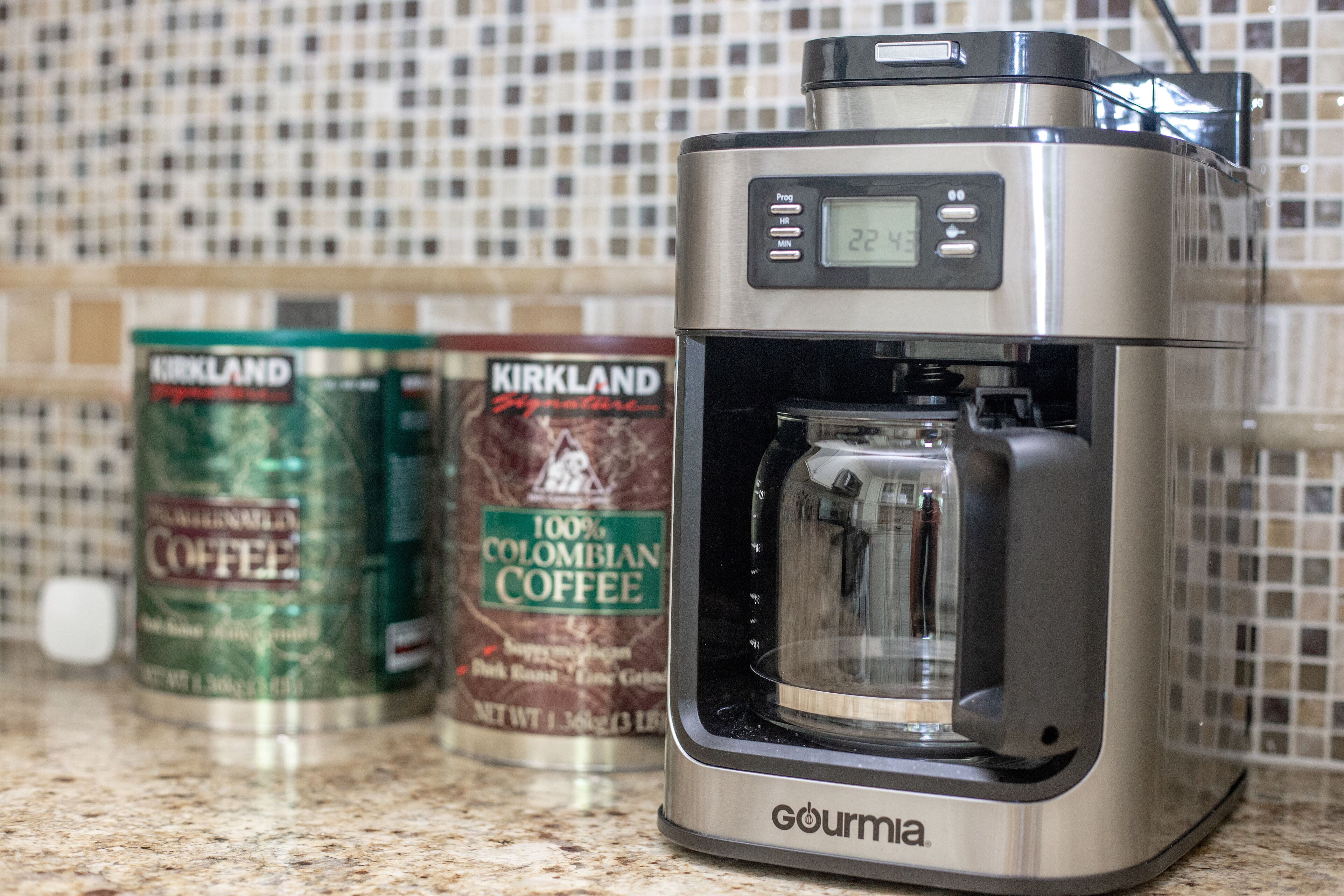 A coffee maker with a digital display, two coffee cans, and a tiled backsplash.