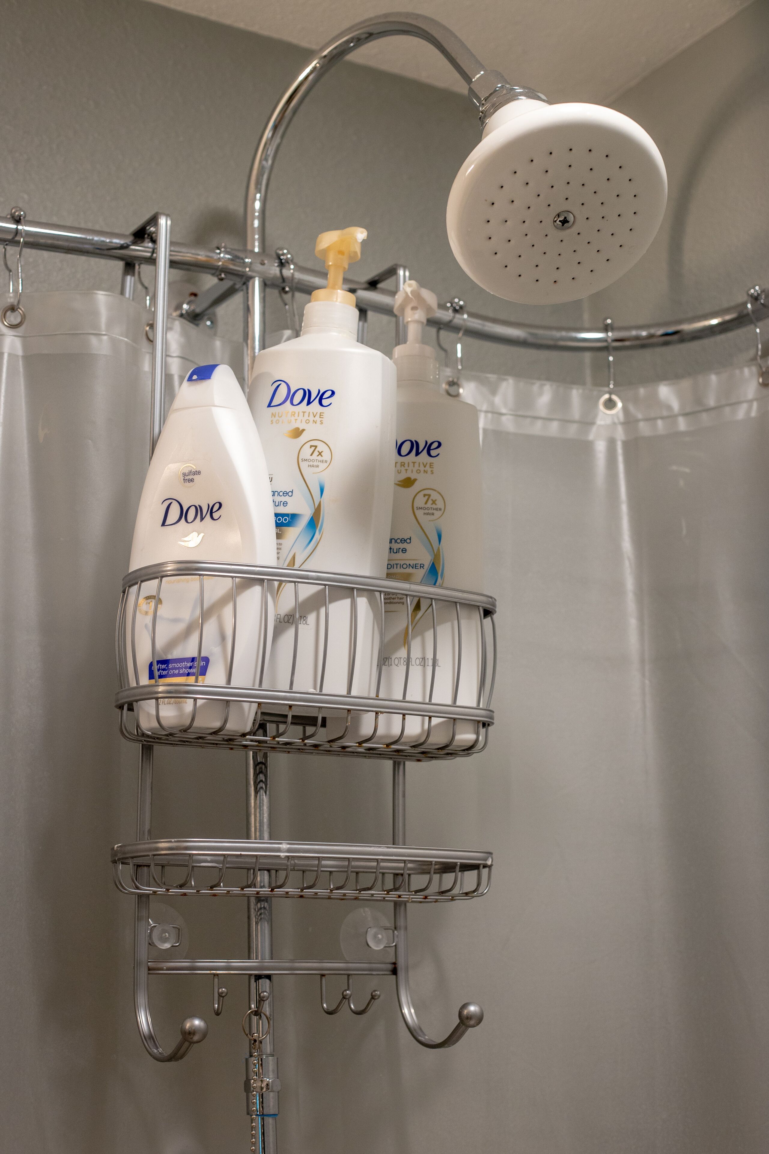 Une salle de bain avec une douche, un présentoir en métal contenant des bouteilles de lotion Dove et un pommeau de douche à main.