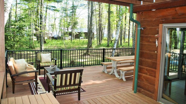 Una terraza de madera con mobiliario exterior, incluyendo un sofá, sillas y una mesa.