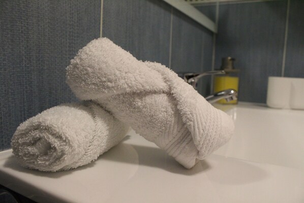 A bathroom with a white sink, a yellow soap dispenser, and a towel rolled up on the sink.