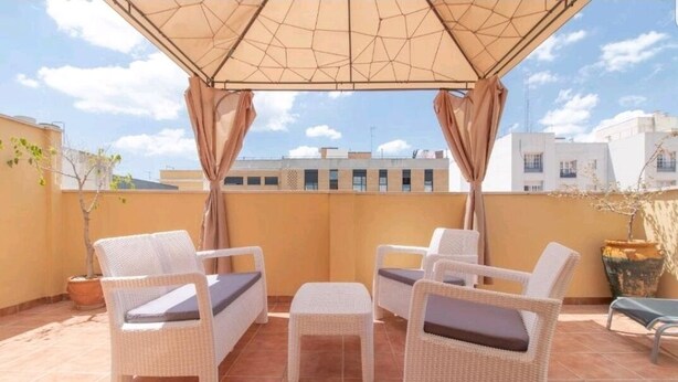 Una terrazza con mobili in vimini, una pergola e vista su edifici sullo sfondo.