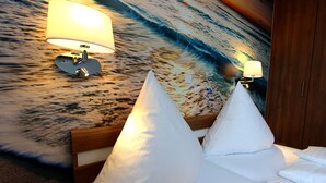 Habitación de hotel con cama, dos almohadas blancas, cabecero de madera, pared con un mural texturizado y dos lámparas de pared.