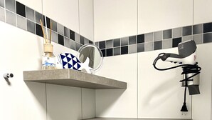 Un baño con paredes de azulejos grises, un lavamanos blanco y un secador de pelo montado en la pared.