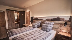 A bedroom with a wooden headboard, a bed with plaid bedding, a nightstand, and a wall-mounted TV. - Raitner Wirt (Schleching)