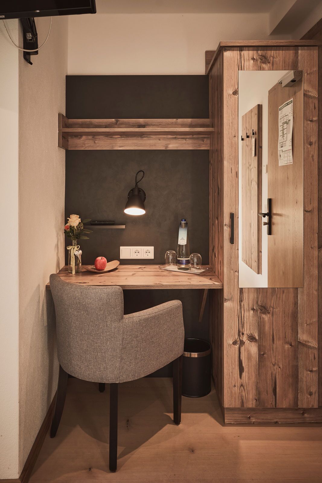 A corner workspace with a desk, chair, lamp, and a wooden cabinet.