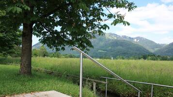 A metal staircase leading down to a stream, surrounded by lush greenery and mountains in the background.