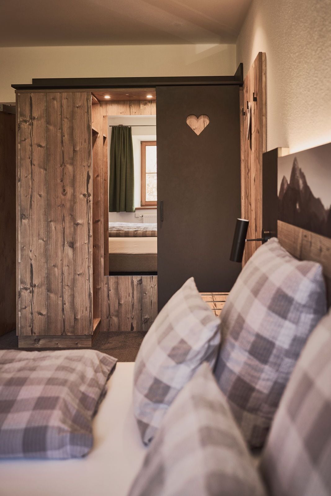 A bedroom with a wooden wardrobe, a bed with plaid bedding, and a heart-shaped decoration on the wall.