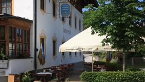An outdoor seating area with tables and chairs, a large umbrella, and a building with ornate decorations and signage.