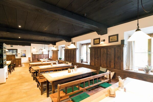 Un restaurante con mesas y bancos de madera, una zona de bar y amplios ventanales que dejan entrar la luz natural.