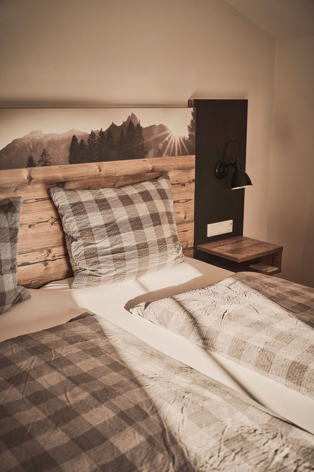 A bedroom with a wooden headboard, a checkered bedspread, and a nightstand with a lamp.