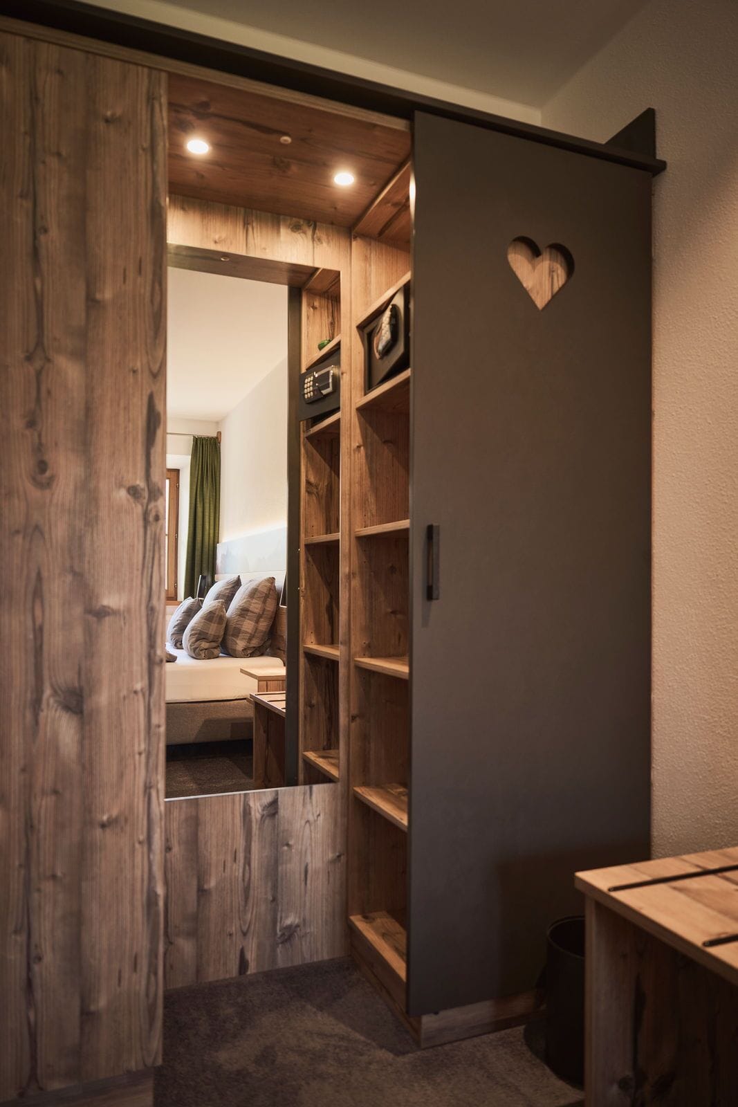 A wooden wardrobe with a heart-shaped decoration on the door, a mirror, and a shelf with various items.