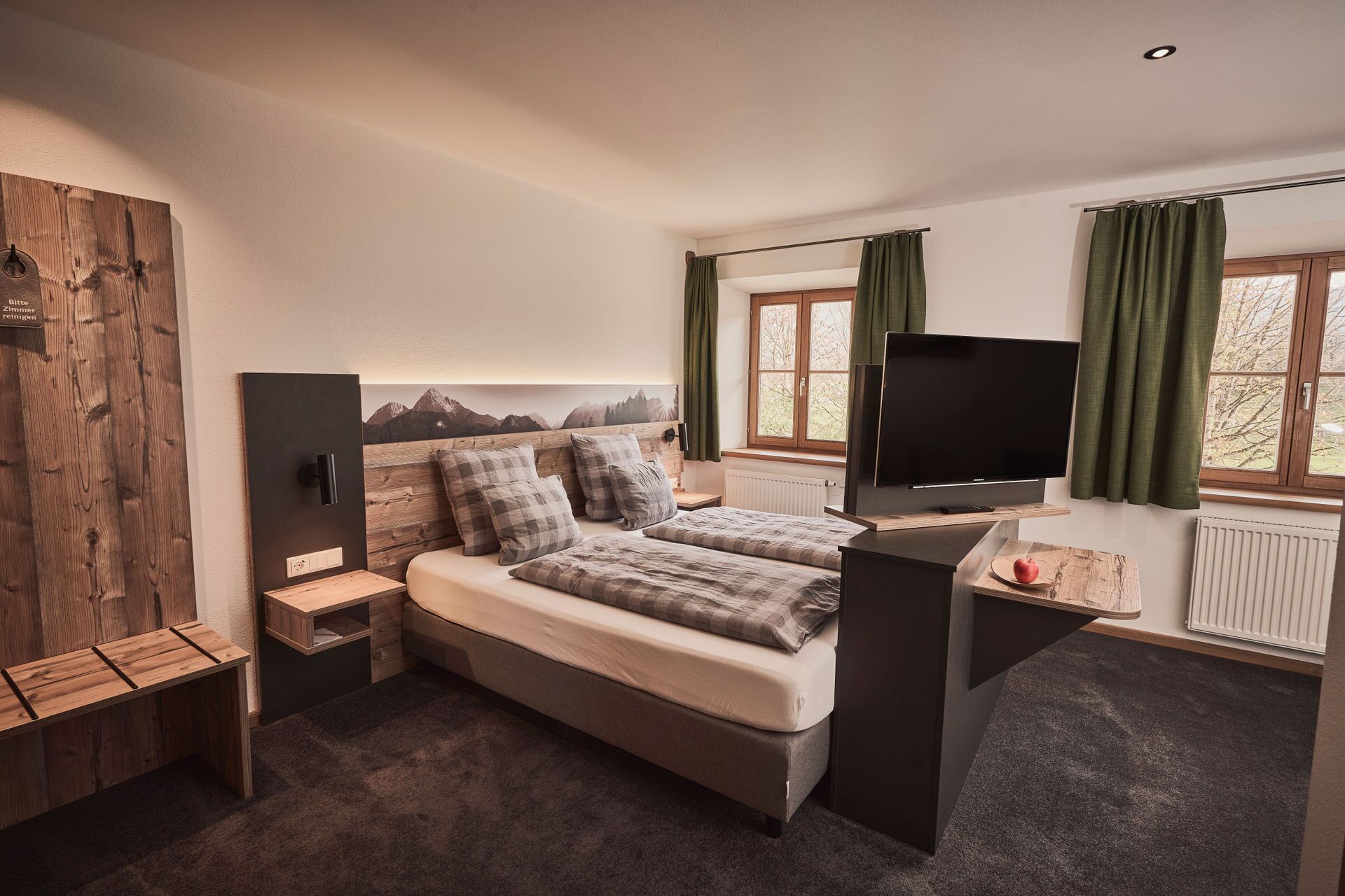A bedroom with a bed, a TV, a desk, and a window with curtains.