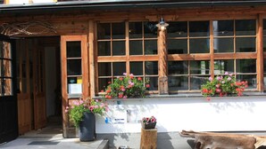 A rustic building with large windows, a wooden porch, and flower planters.