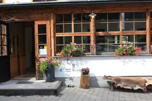 A rustic building with large windows, a wooden porch, and flower planters.