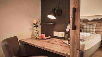 Une chambre confortable avec un bureau en bois, une chaise, une table de chevet avec une lampe, un vase de fleurs et un lit donnant sur une vue sur les montagnes.
