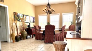 A spacious living room with a tiled floor, a chandelier, and a dining area with red patterned chairs.