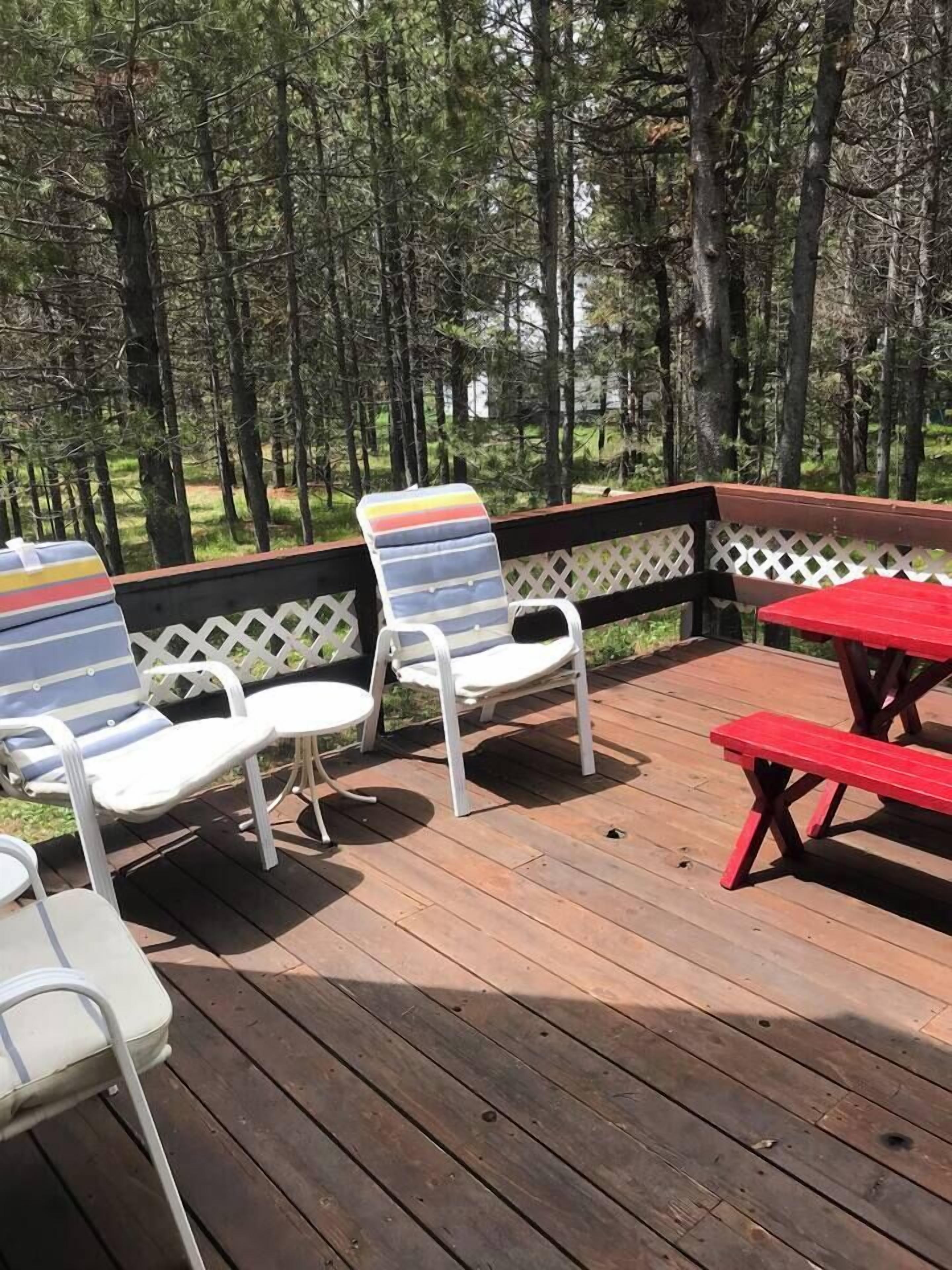 A deck with white and striped lounge chairs, a red picnic table, and a white lattice railing.