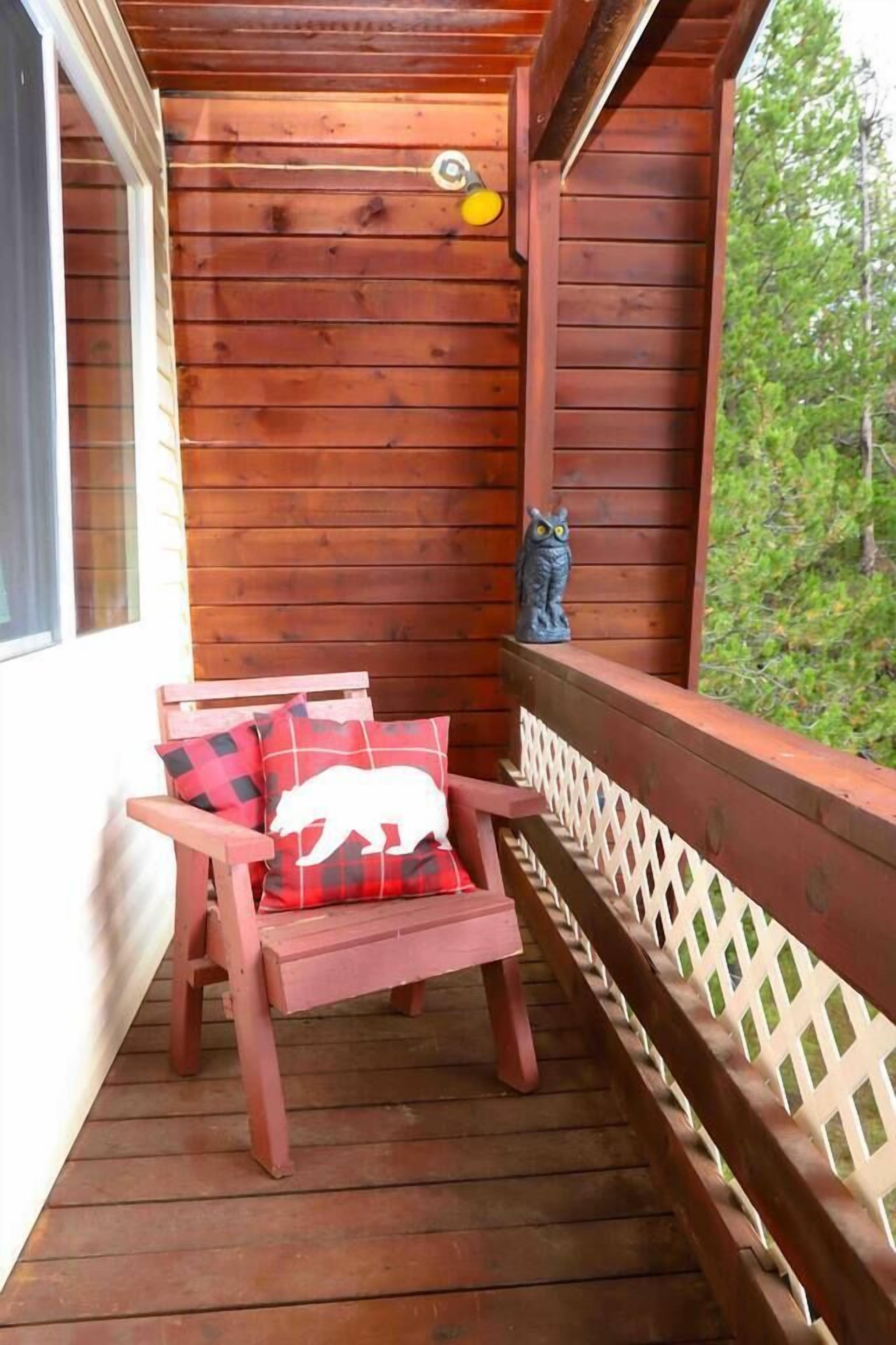 A wooden deck with a red chair and a white bear pillow, a small owl statue, and a white lattice railing.