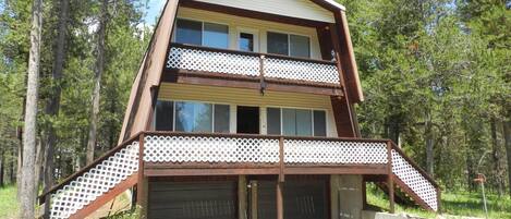 A two-story cabin with a balcony, surrounded by trees.