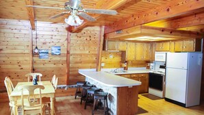 Interior de una cabaña de madera con una cocina que incluye una isla central, una mesa de comedor de madera y sillas.