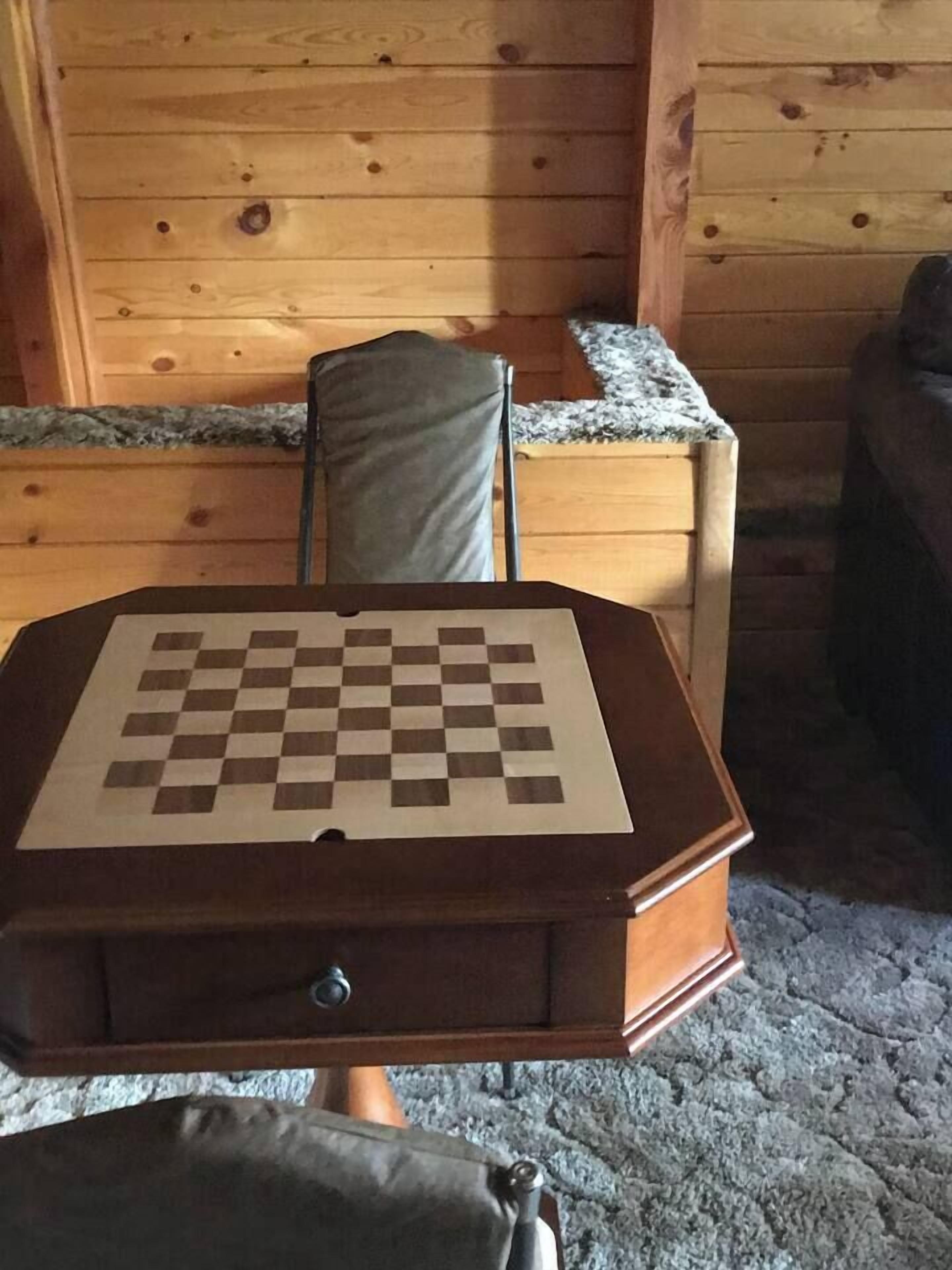 Ein Holztisch mit einem Schachbrett, ein Stuhl und eine Holzkommode in einem Zimmer mit Holzwänden.