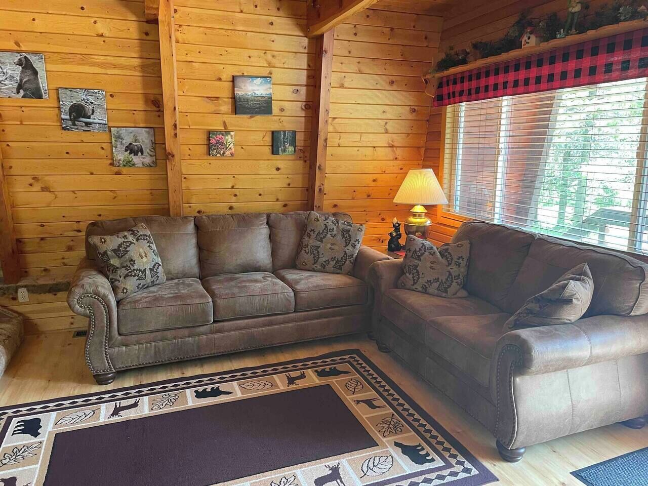 Una sala de estar acogedora con dos sofás y un tapete con estampados de animales, paredes de madera y una ventana con persianas.